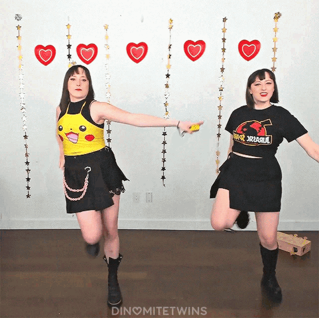 two women are dancing in front of a wall with hearts and stars and the words dinomitetwins on the bottom