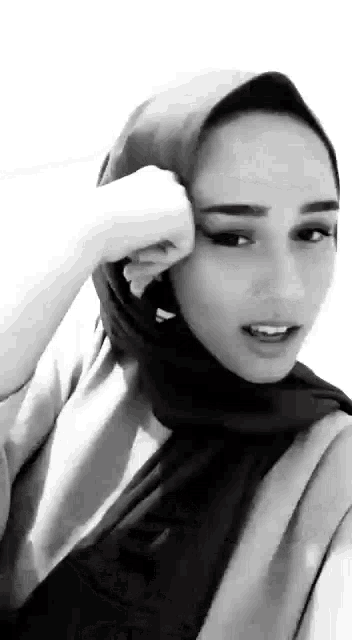 a black and white photo of a woman wearing a hijab and covering her face .
