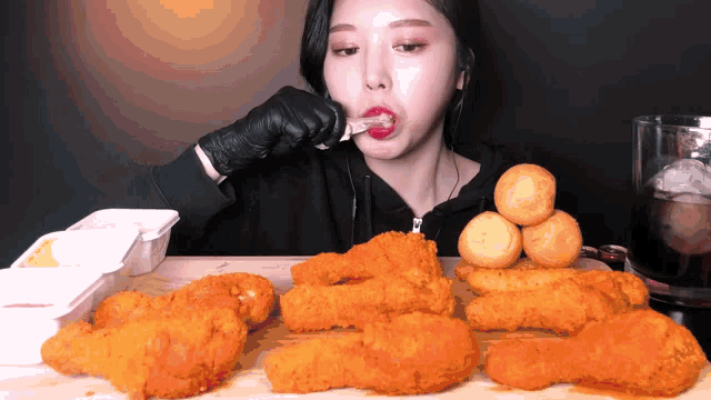 a woman wearing black gloves is eating fried chicken with a fork