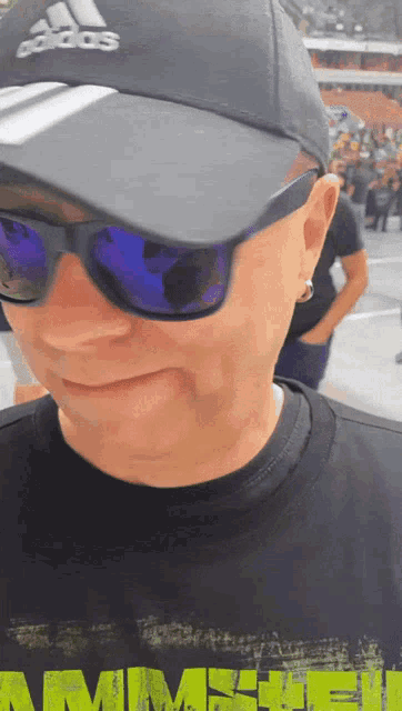 a man wearing sunglasses and an adidas hat stands in front of a crowd