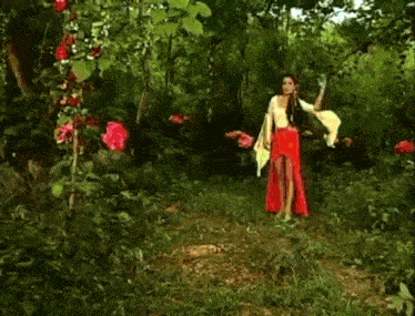 a woman in a red dress is standing in the middle of a forest with a light coming out of her hand .