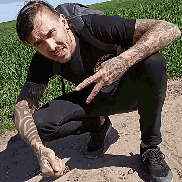 a man with a tattoo on his arm is squatting down in a field
