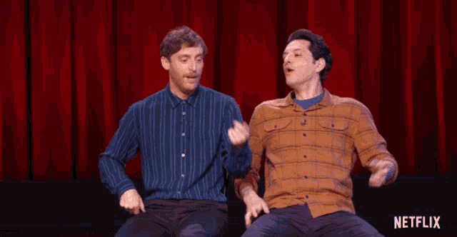 two men are sitting in front of a red curtain with a netflix logo