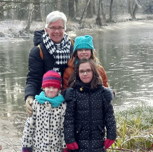 a woman and three girls are posing for a picture in front of a body of water