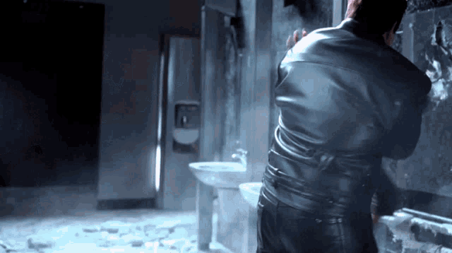 a man in a leather jacket stands in a bathroom