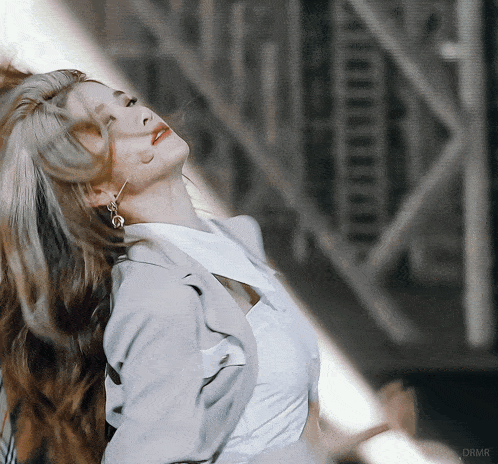 a woman in a white shirt and gray jacket is looking up with the watermark drmr