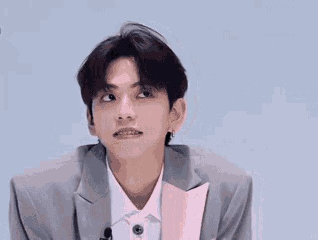 a young man wearing a suit and a pink jacket is sitting in front of a microphone .