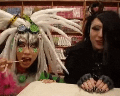 a woman with long black nails is eating a lollipop next to another woman