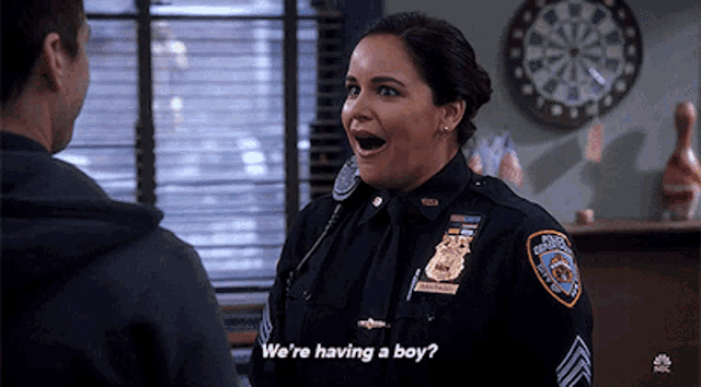 a woman in a police uniform is talking to a man and says we 're having a boy .