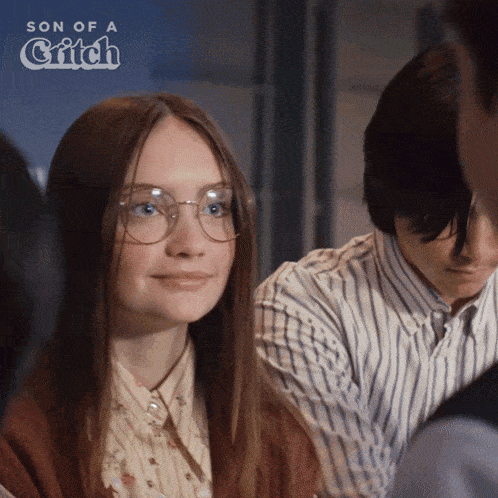 a woman wearing glasses is smiling in front of a sign that says son of a critch