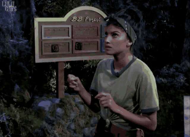 a woman in a green shirt is standing in front of a sign that says bb forest