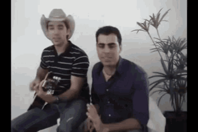 a man in a cowboy hat sits next to another man with a guitar