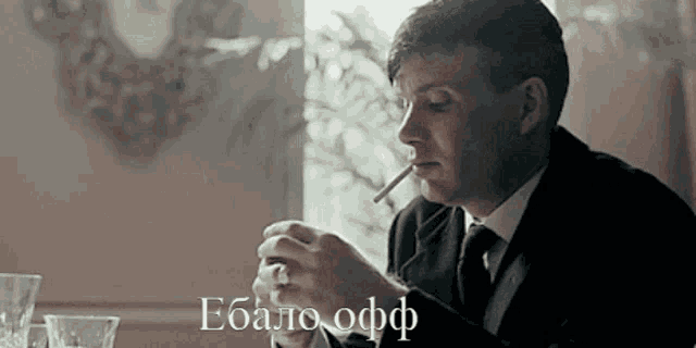 a man in a suit and tie is smoking a cigarette while sitting at a table .