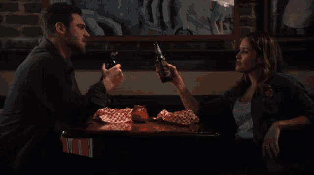 a man and woman are sitting at a table with a bottle of beer