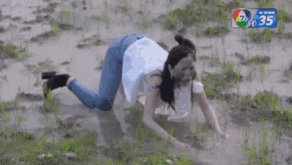a woman is crawling through a muddy field with the number 35 on the bottom of the screen .