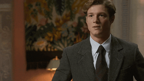 a man in a suit and tie stands in front of a tapestry