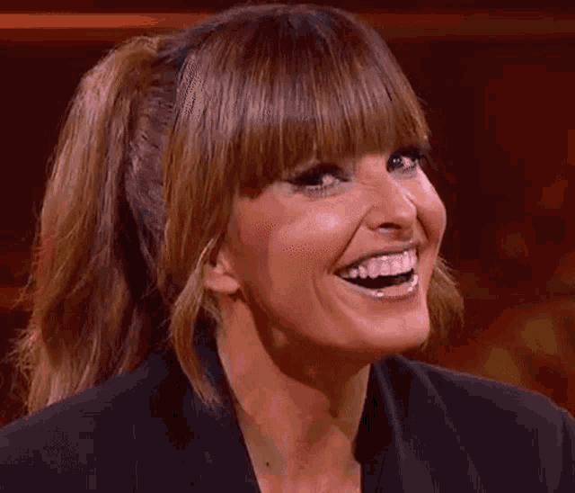 a woman with a ponytail and bangs is laughing with her mouth wide open .