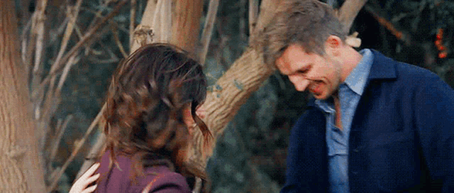 a man and woman are standing next to each other in a forest .