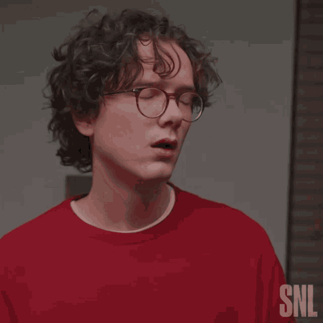 a man wearing glasses and a red shirt with snl on it