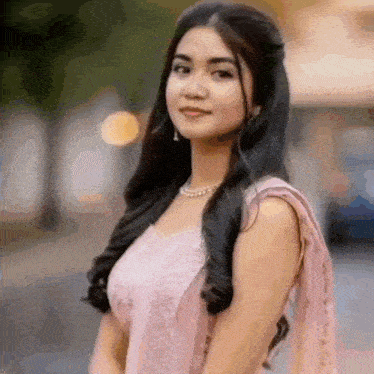 a woman in a pink dress and a pearl necklace is standing in front of a blurry background .