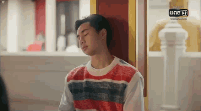 a young man in a striped sweater is leaning against a red wall .