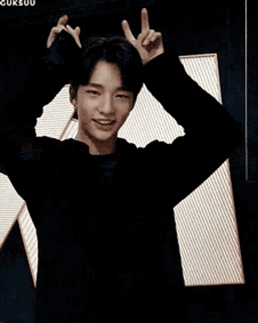 a young man in a black jacket is smiling and waving his hands in the air