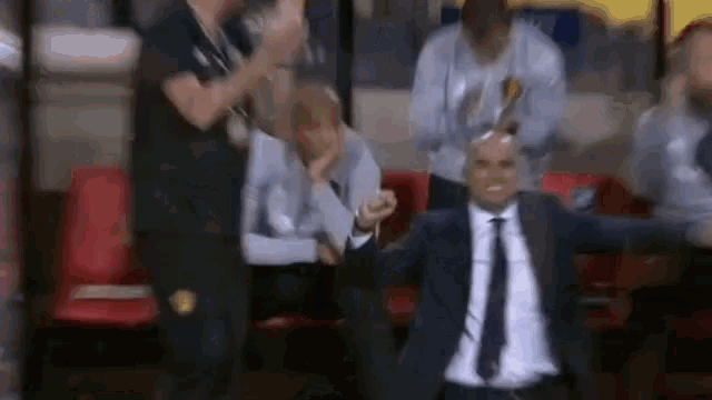 a man in a suit and tie is sitting in a stadium with his arms outstretched