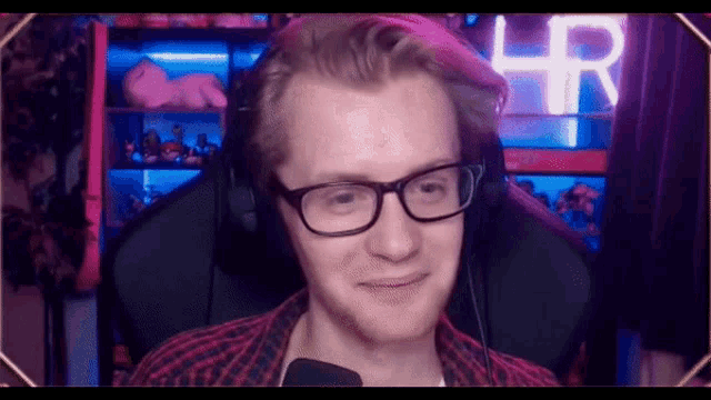 a man wearing glasses and headphones is sitting in front of a microphone and smiling .