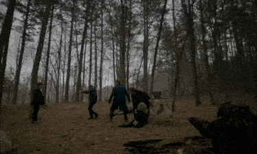 a man in a black coat holds a gun in front of a police officer in the woods
