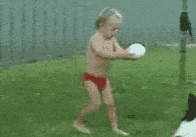 a boy in red swim trunks is running towards a white ball