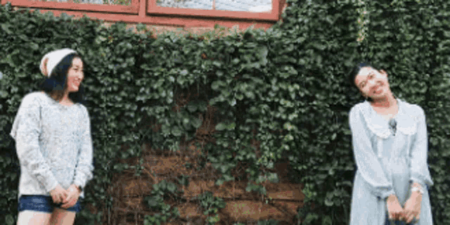 two young women are standing next to each other in front of a ivy covered wall .