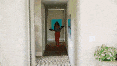 a woman is walking down a hallway with a picture on the wall behind her