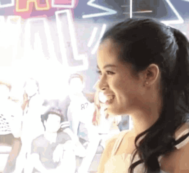 a woman with a ponytail is smiling in front of a neon sign that says ' a ' on it .