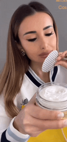 a woman is holding a jar of cream in her hand and applying it to her face .