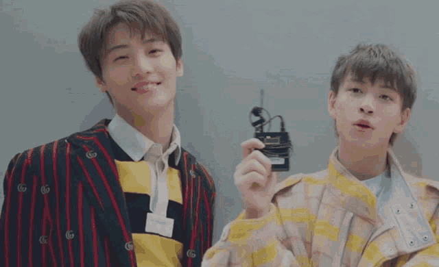 two young men are standing next to each other and one of them is holding a small device that says ' g ' on it