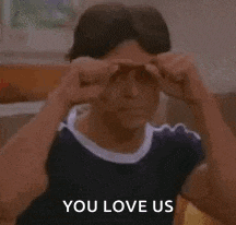 a young man is pointing at his face and saying `` you love us '' while sitting on a couch .