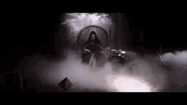 a woman in a black dress is sitting in a chair surrounded by fog