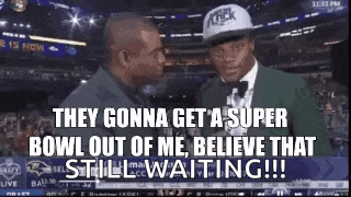 a man in a hat is talking to another man in a suit at a football game .
