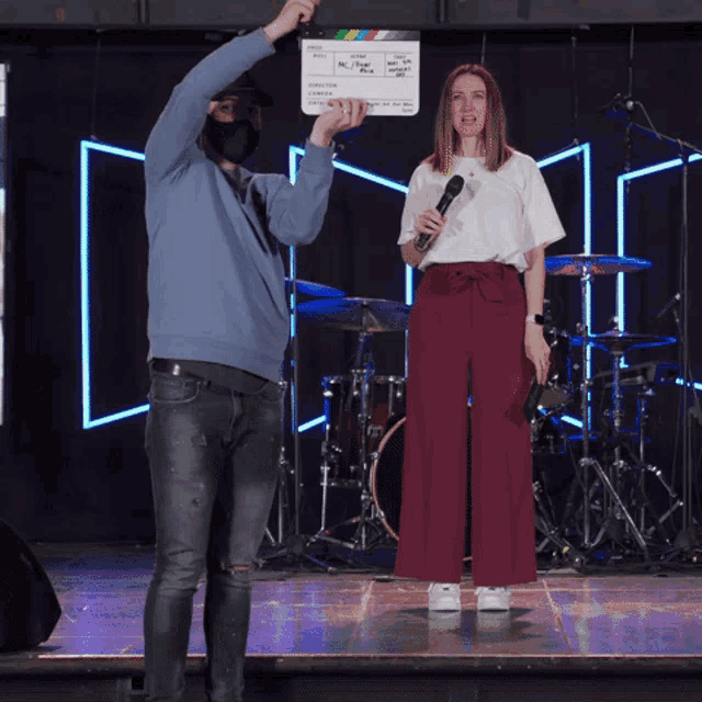 a man holds up a clapper board that says ' casting call ' on it above a woman holding a microphone