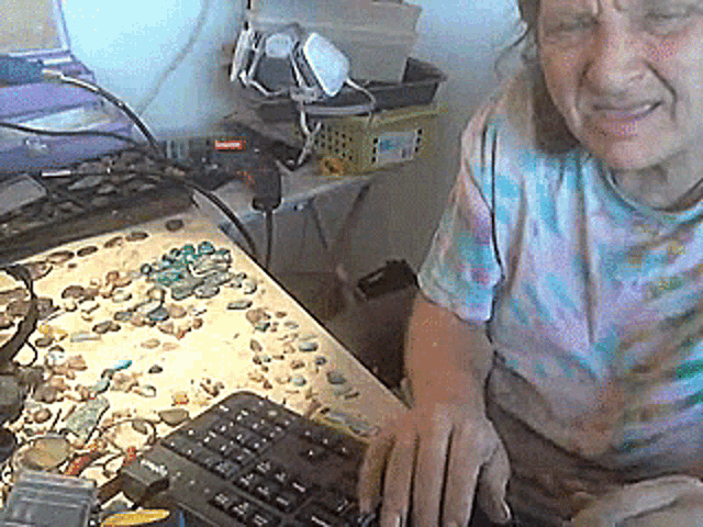 a woman in a tie dye shirt sits at a desk in front of a keyboard