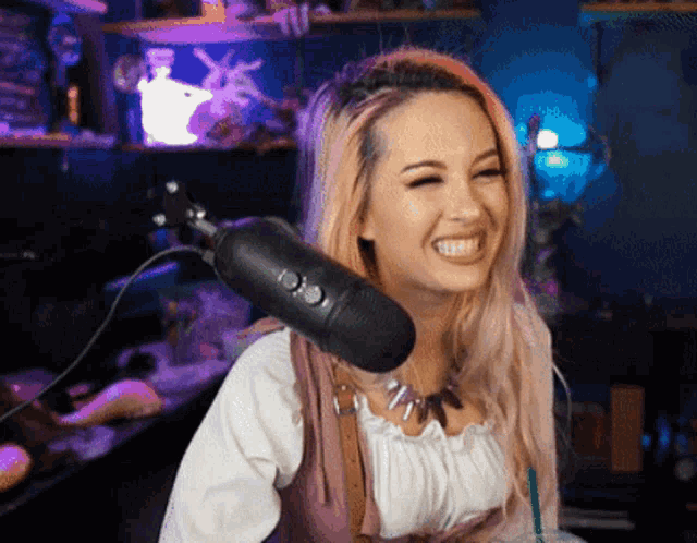 a woman with pink hair is laughing in front of a microphone with a purple background
