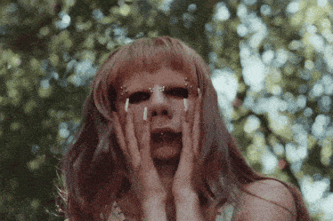 a woman with red hair and piercings on her face is covering her face with her hands