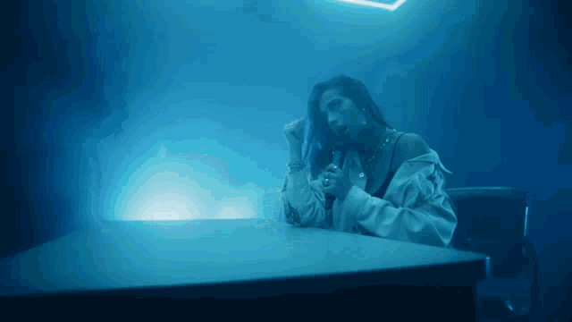 a woman sitting at a table in a dark room with blue lights behind her