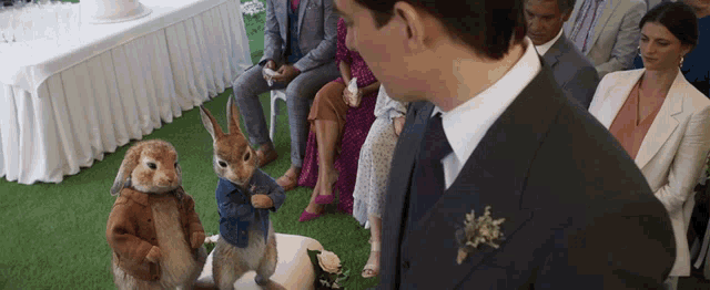 a man in a suit stands in front of a group of people including a stuffed rabbit