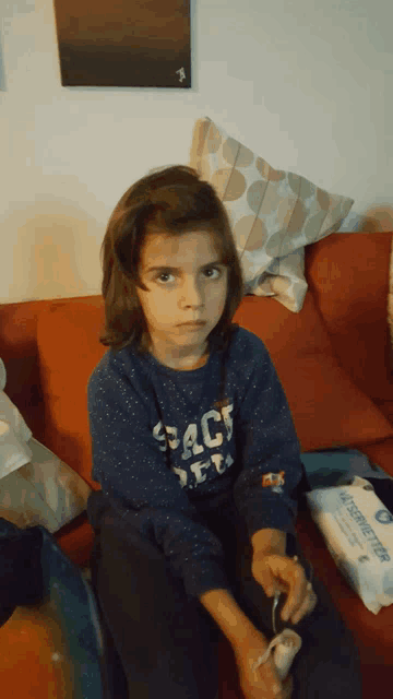 a little girl is sitting on a couch wearing a space shirt