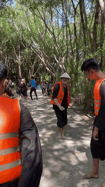 a group of people wearing orange life vests are standing on a path in the woods