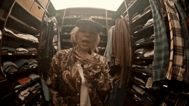 a woman in a paisley shirt is standing in a closet filled with clothes