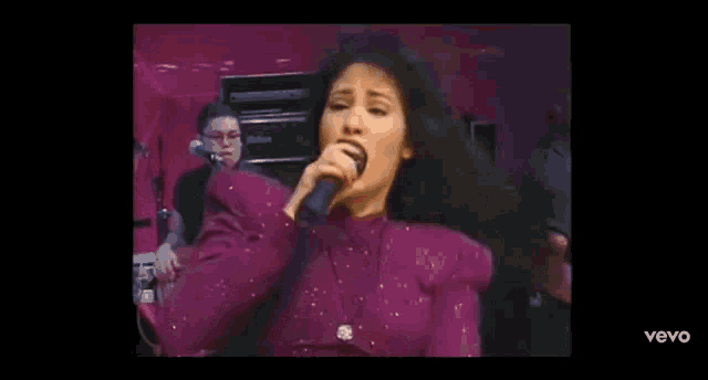 a woman is singing into a microphone while a man plays drums in the background .
