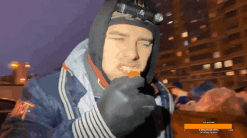 a man wearing a hooded jacket is eating a piece of food