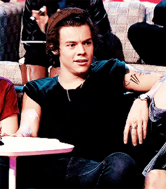 a man with a tattoo on his arm is sitting on a couch with other people